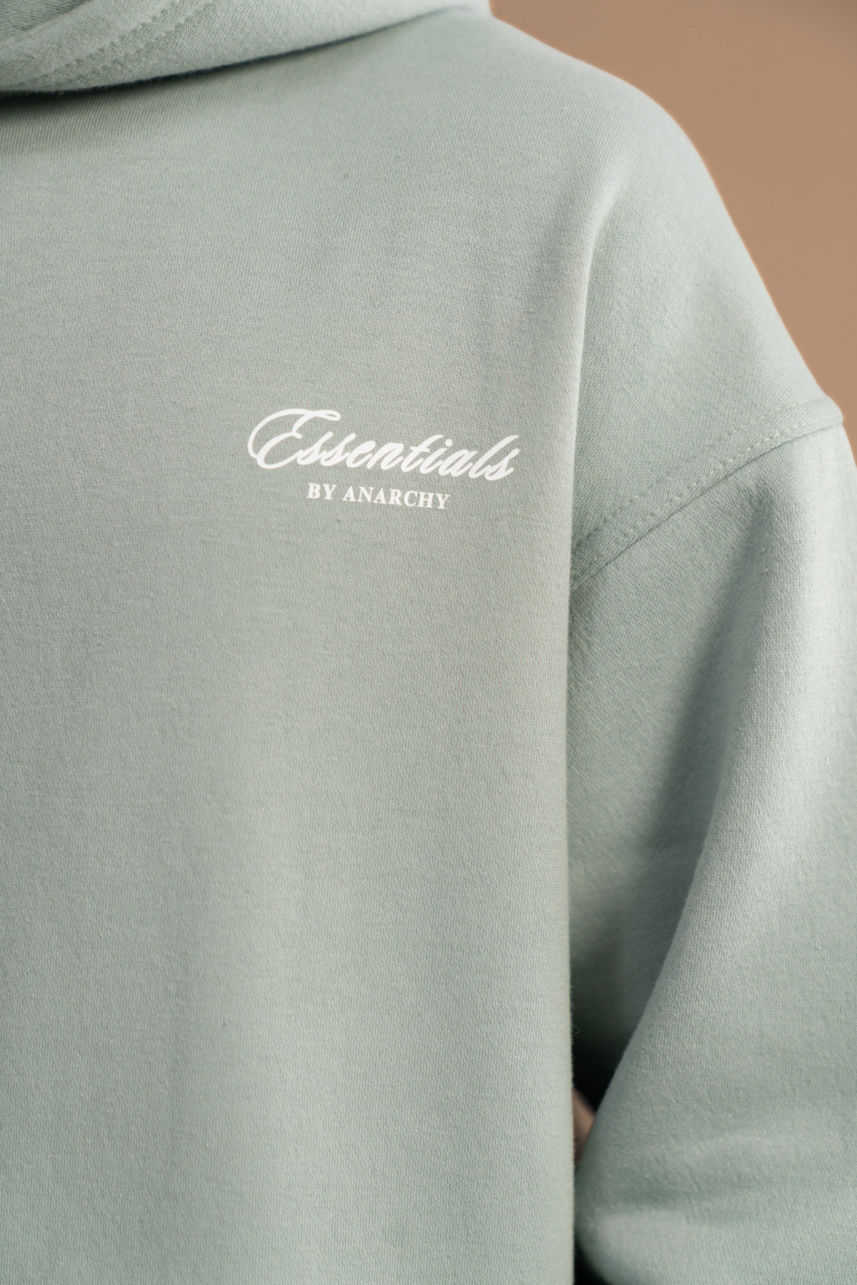 Close-up of Wear Anarchy Aqua Green Essential Hoodie showing Essentials by Anarchy embroidered chest logo and fabric texture
