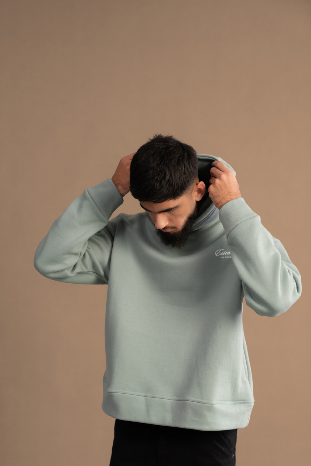 Wear Anarchy Aqua Green Essential Hoodie for men adjusting the hood, featuring a relaxed fit and embroidered chest logo