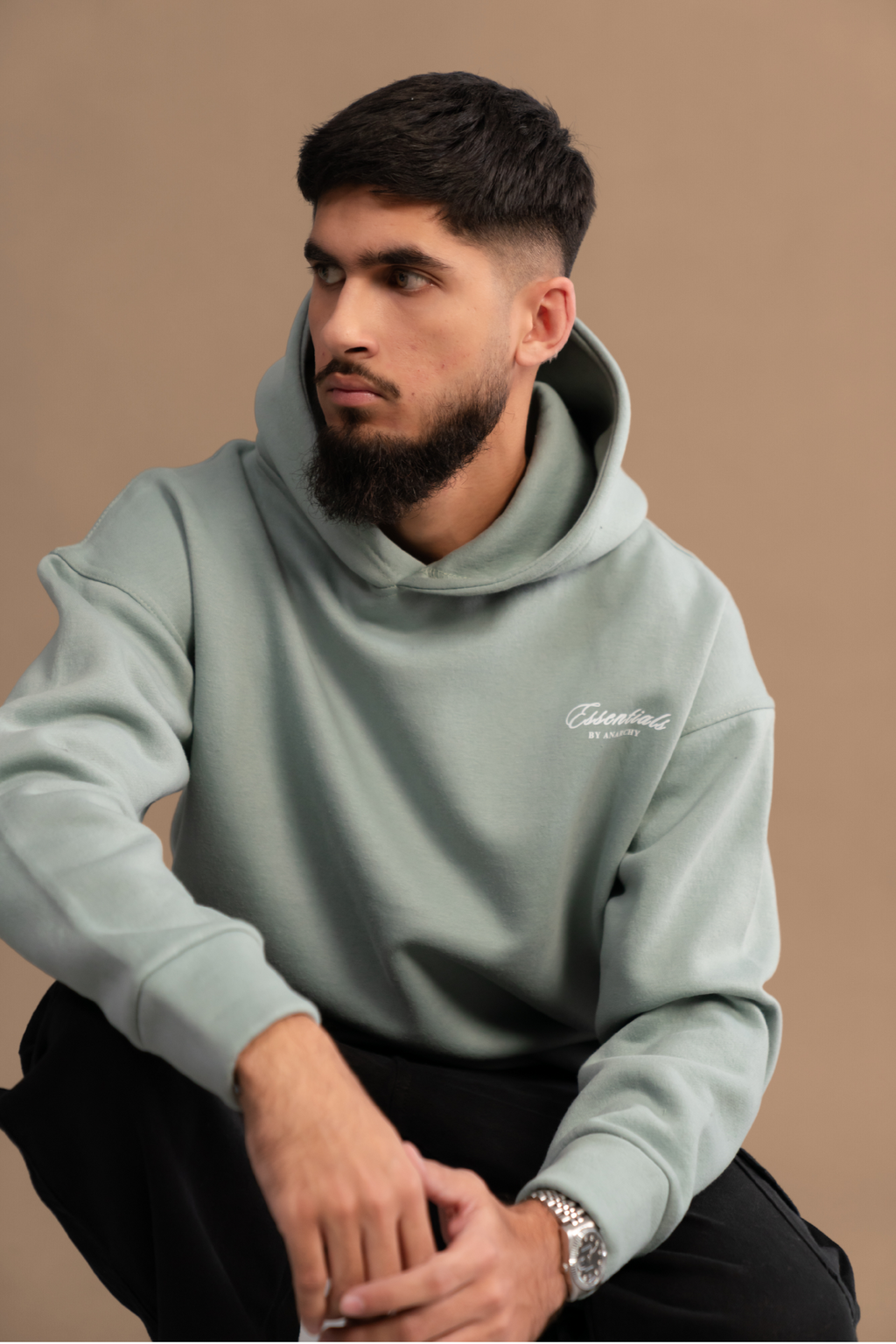 Wear Anarchy Aqua Green Essential Hoodie for men in a seated close-up showing relaxed fit, hood and embroidered chest logo