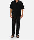 Wear Anarchy black short-sleeve button-up shirt for men styled with black trousers and sandals