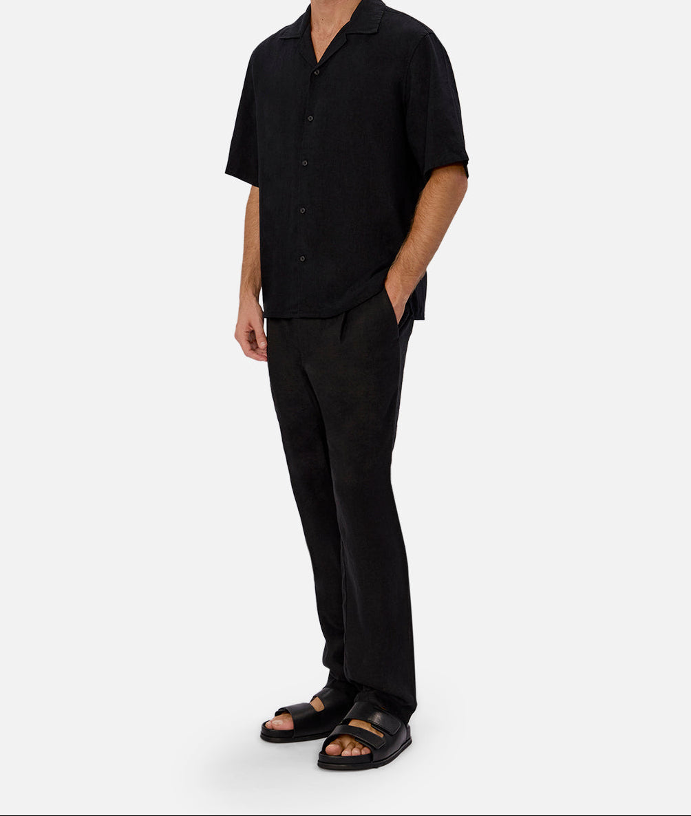 Three-quarter view of Wear Anarchy black short-sleeve button-up shirt for men styled with black trousers and sandals