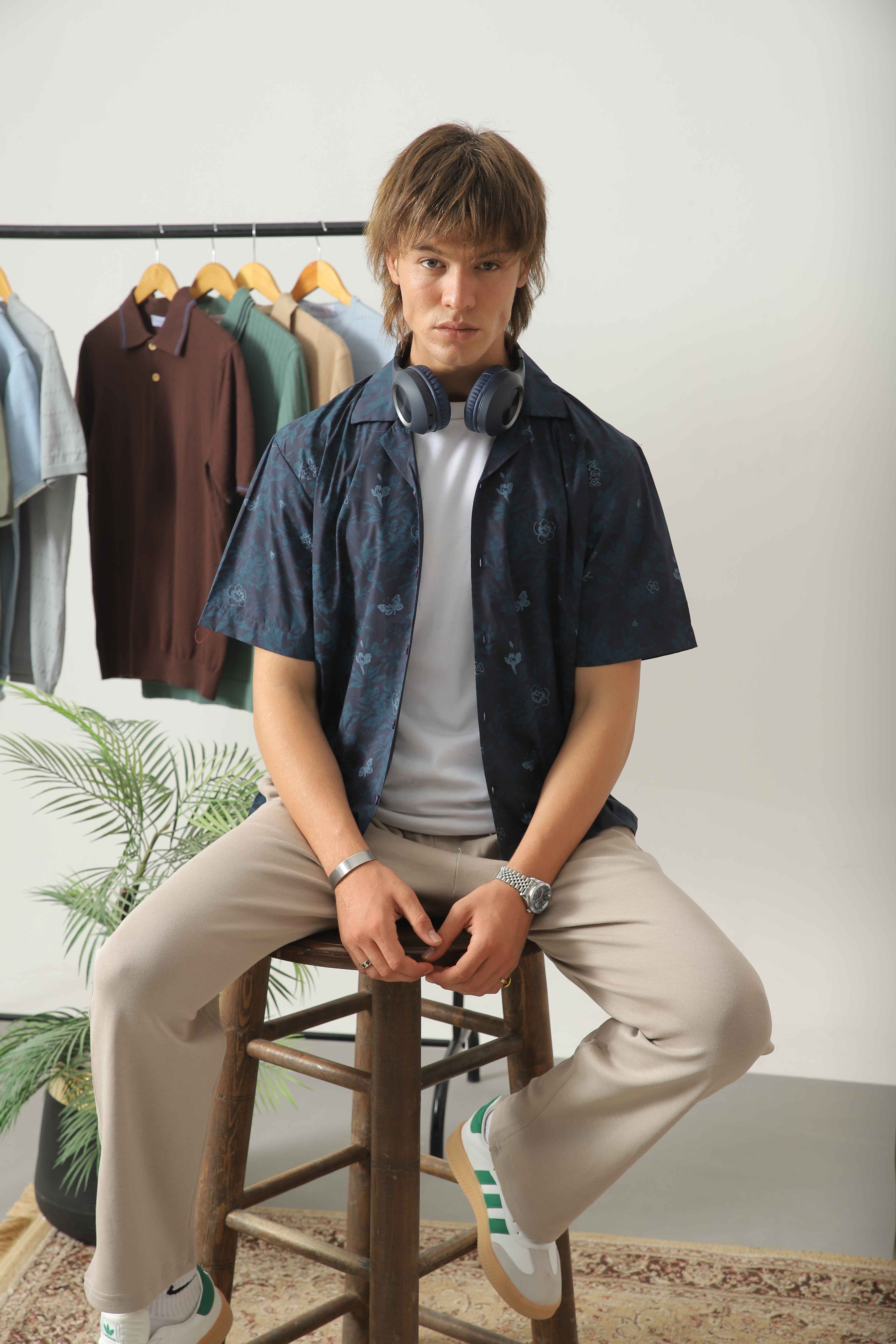 Wear Anarchy blue print resort shirt for men layered over a white t-shirt and styled with beige trousers in a seated look