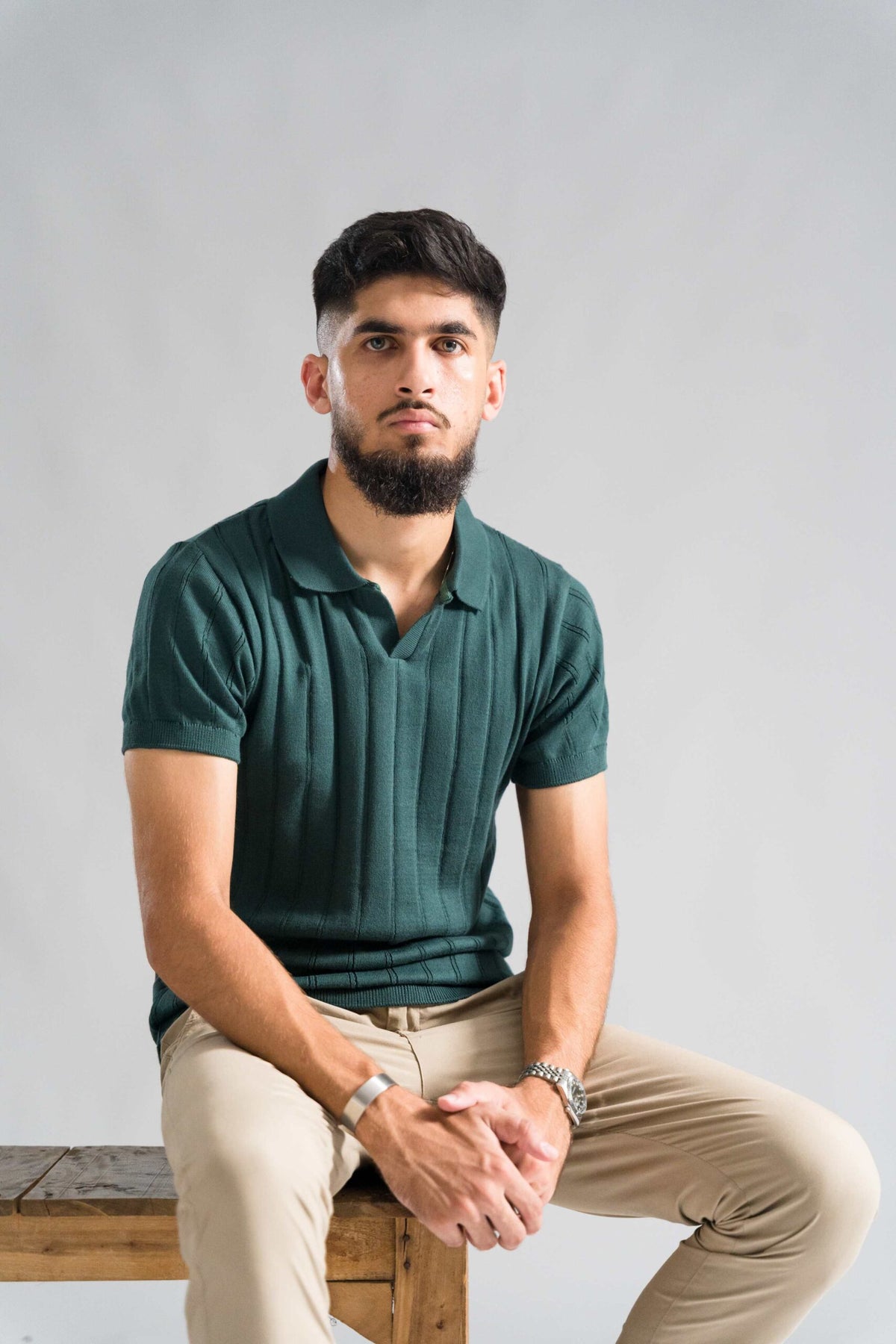 Wear Anarchy Forest Green Knitted Polo for men styled with beige trousers in a relaxed seated look