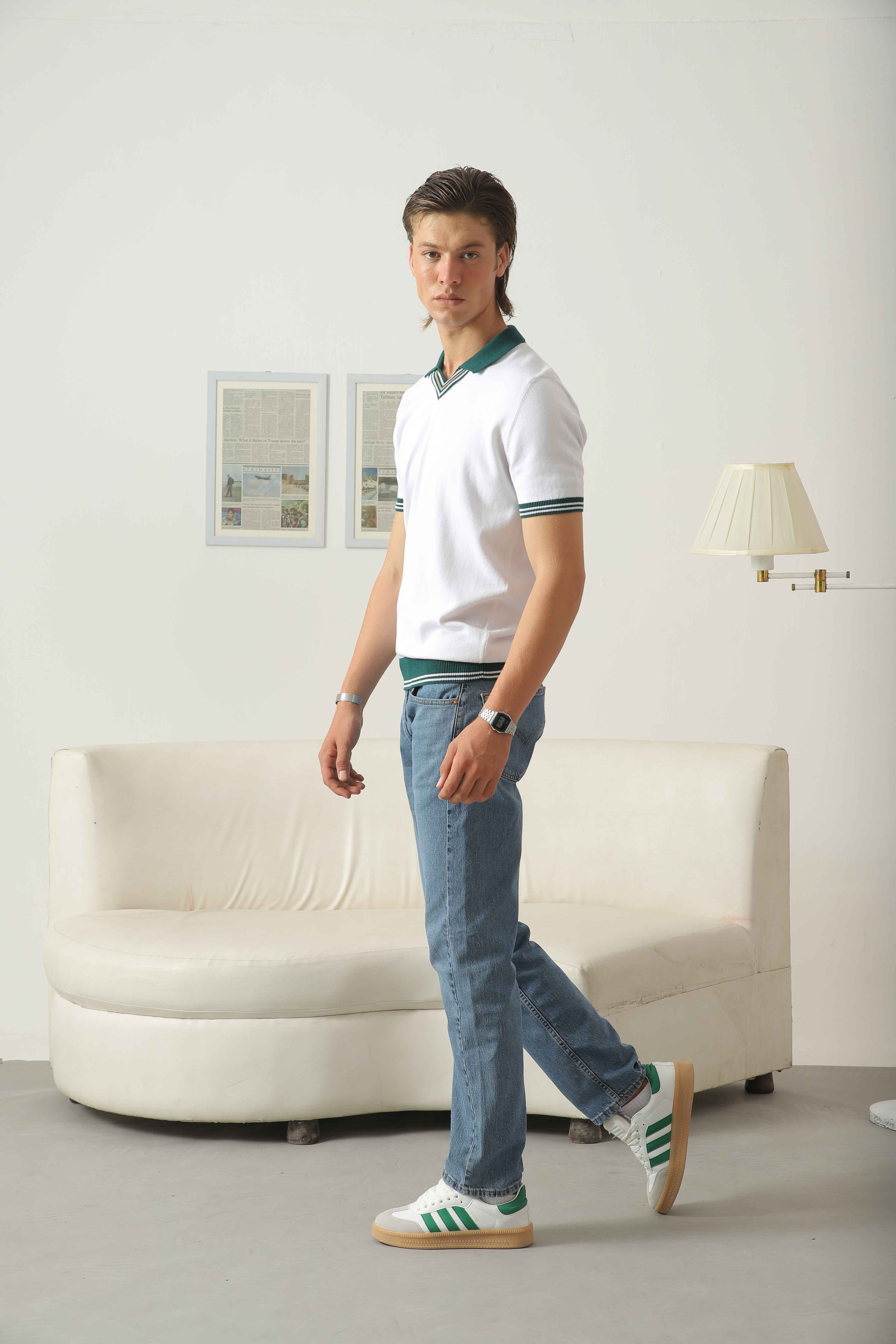 Walking side view of Wear Anarchy white knit polo shirt for men with green contrast collar and striped trim styled with blue jeans and sneakers